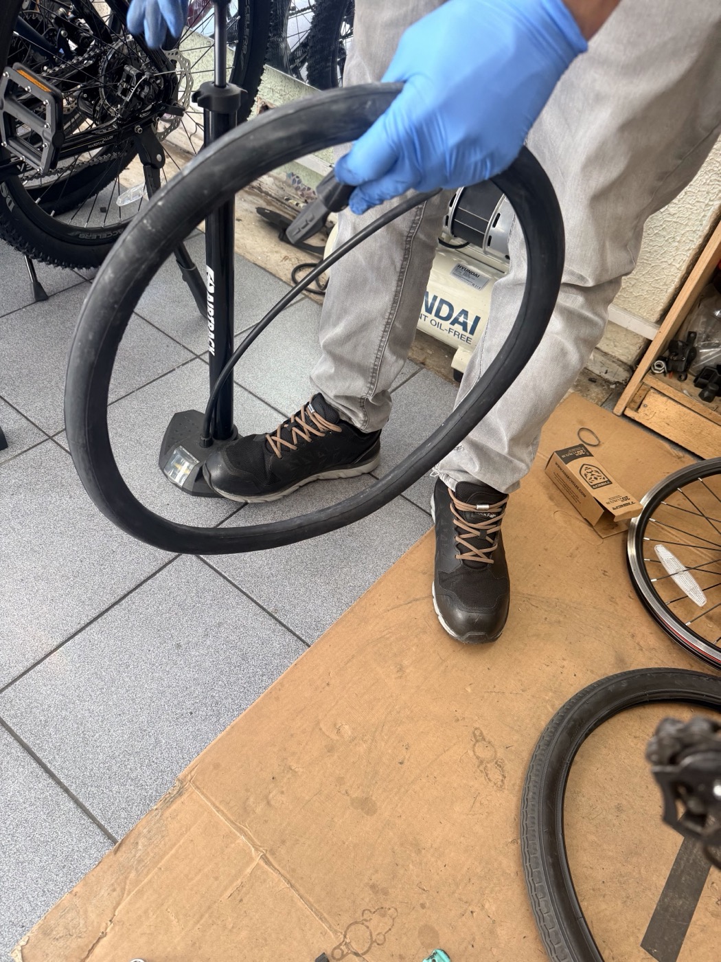 A mechanic in blue gloves inflating and checking an inner tube during a repair at Bethnal Green Cycles.